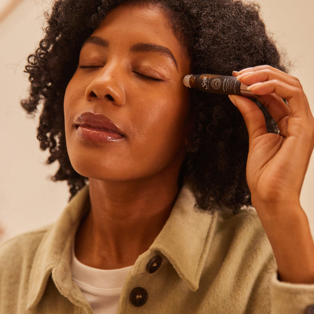 Woman applying a roll-on to her temple with her eyes closed